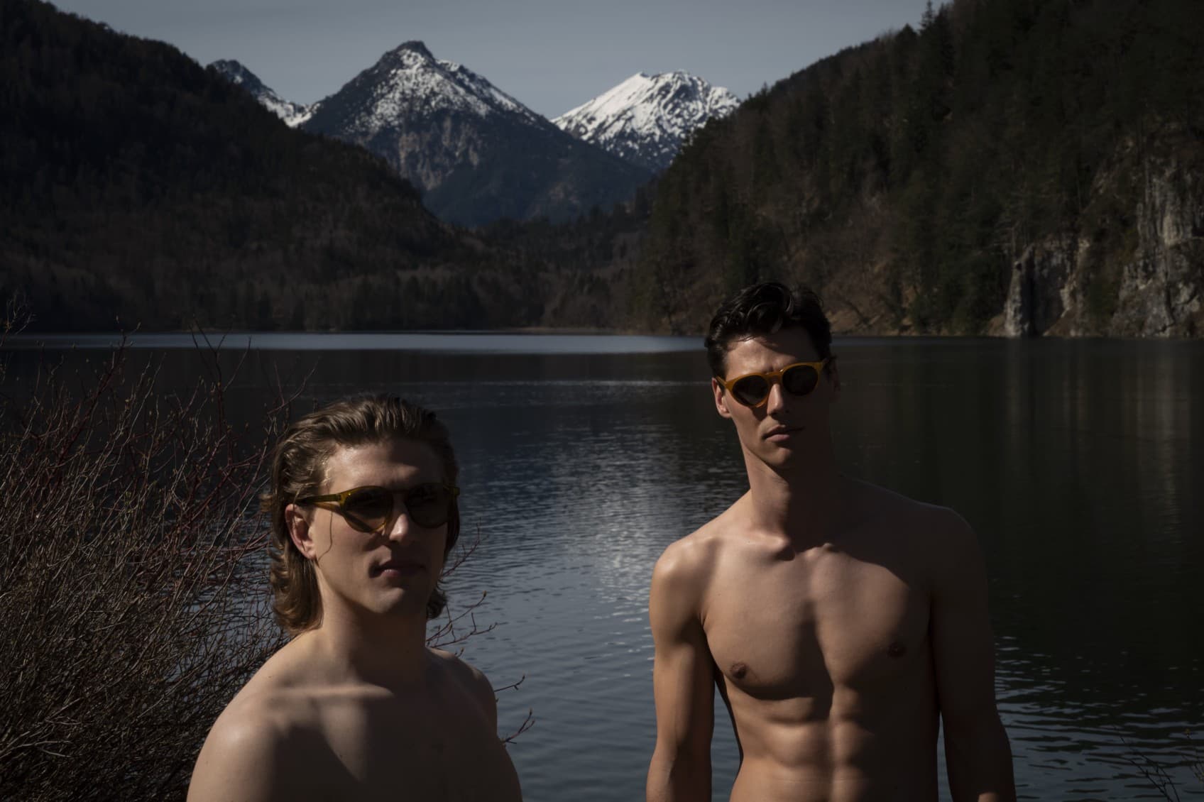 Two men stand with their upper bodies exposed in front of a lake in the Bavarian Alps