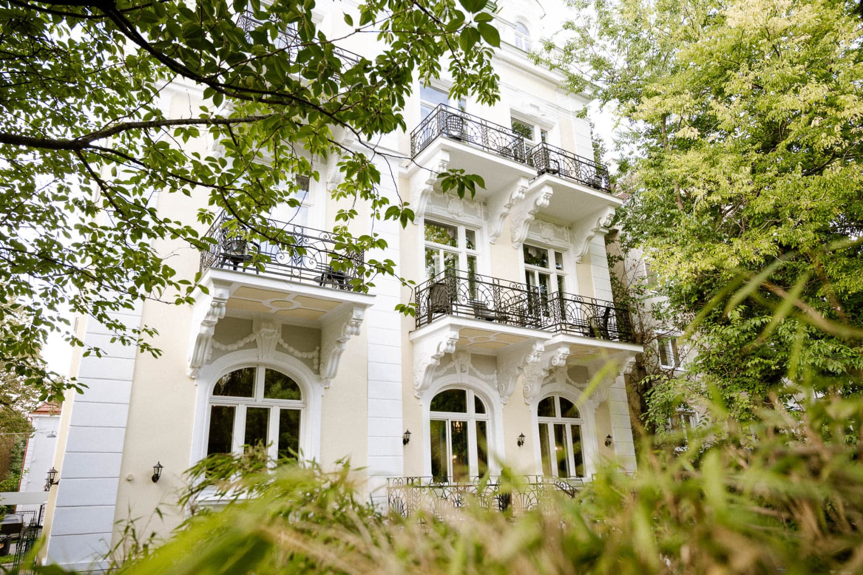 Gezeigt wird die Außenansicht des Hideauts Hotels Villa R, das sich durch seine wunderschön zum Garten hin gelegenen Balkone auszeichnet.