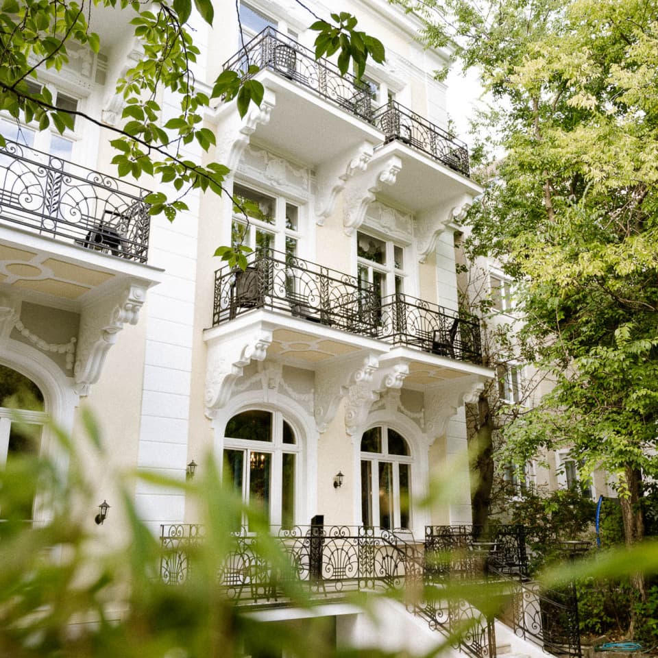 Zu sehen ist die Außenseite der Villa R mit Blick auf die Rückseite der Villa und die Balkone. Durch den Garten hindurch fotografieren.